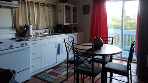 A compact kitchen with a stove, sink, and cabinets, a dining table with chairs, and a view of greenery through a window. - The Cottage at Villa Indigo 2BR/1.5BA in Exclusive Private Gated Community (Saint Thomas)