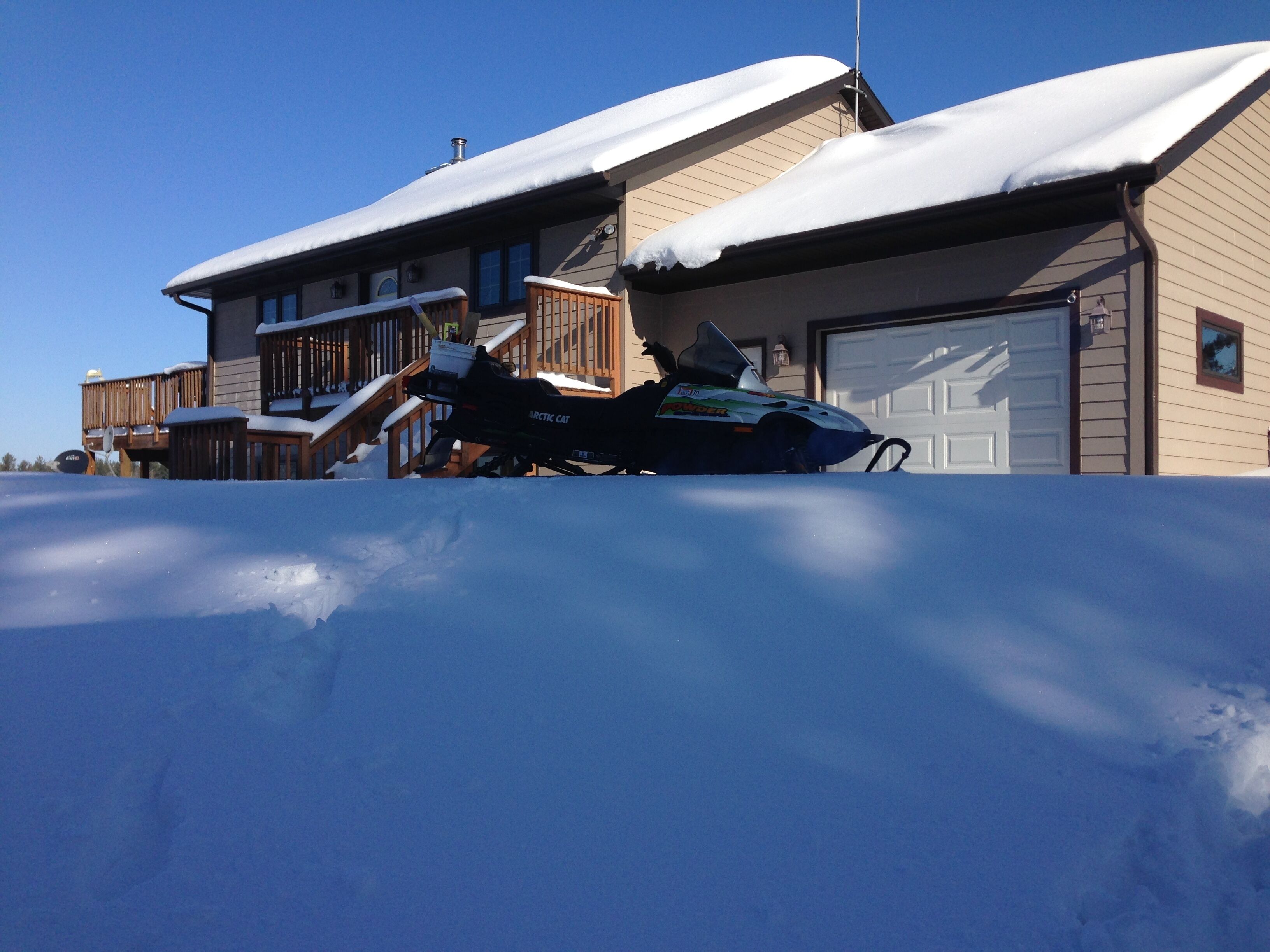 A snow-covered house with a snowmobile parked in front.
