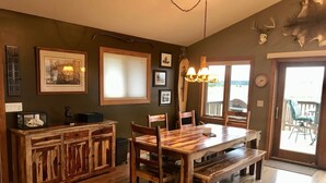 Un coin repas avec une table et des bancs en bois, des tableaux encadrés aux murs et un lustre.