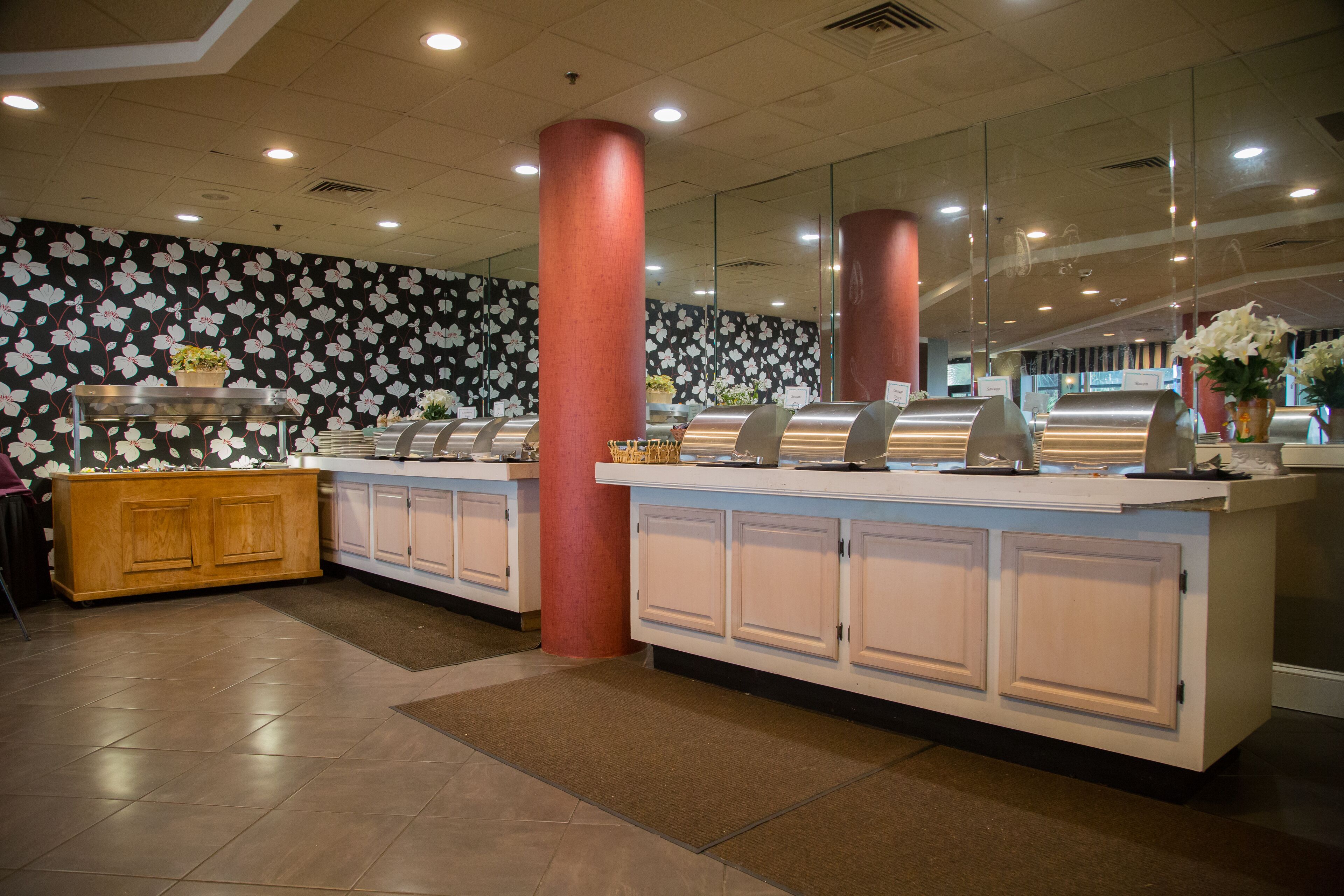 Un espace buffet agrémenté d’un mur décoré de motifs floraux, d’un meuble en bois et d’un pilier rouge.