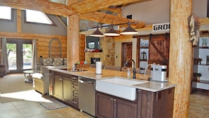 A spacious kitchen with a large island, wooden beams, and a stone wall. - Private Pool & Hot Tub Near Lake LBJ | 3 King Bedrooms, Sleeps 13 (Burnet)