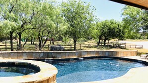A swimming pool with a stone border and a circular hot tub, surrounded by trees and a wooden fence. - Private Pool & Hot Tub Near Lake LBJ | 3 King Bedrooms, Sleeps 13 (Burnet)
