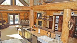 A log cabin interior with a kitchen, dining area, and a fireplace. - Private Pool & Hot Tub Near Lake LBJ | 3 King Bedrooms, Sleeps 13 (Burnet)