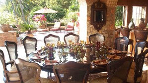 Un espace extérieur aménagé pour les repas, avec une table ronde dressée pour un repas, entourée de chaises en osier.