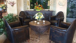 Un espace détente avec des fauteuils en cuir, une table ronde et un décor composé de fleurs et d’un mur en pierre.