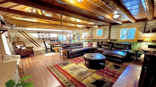 Un salón amplio con un sofá seccional grande, una mesita de centro y una zona de comedor con una mesa y sillas de madera.