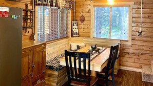 Una cocina acogedora de estilo rústico con paredes de madera, una mesa de comedor con sillas, un refrigerador y un reloj.