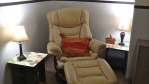 Een verstelbare fauteuil met voetbank, twee kleine tafels met lampen, en een rood vloerkleed.
