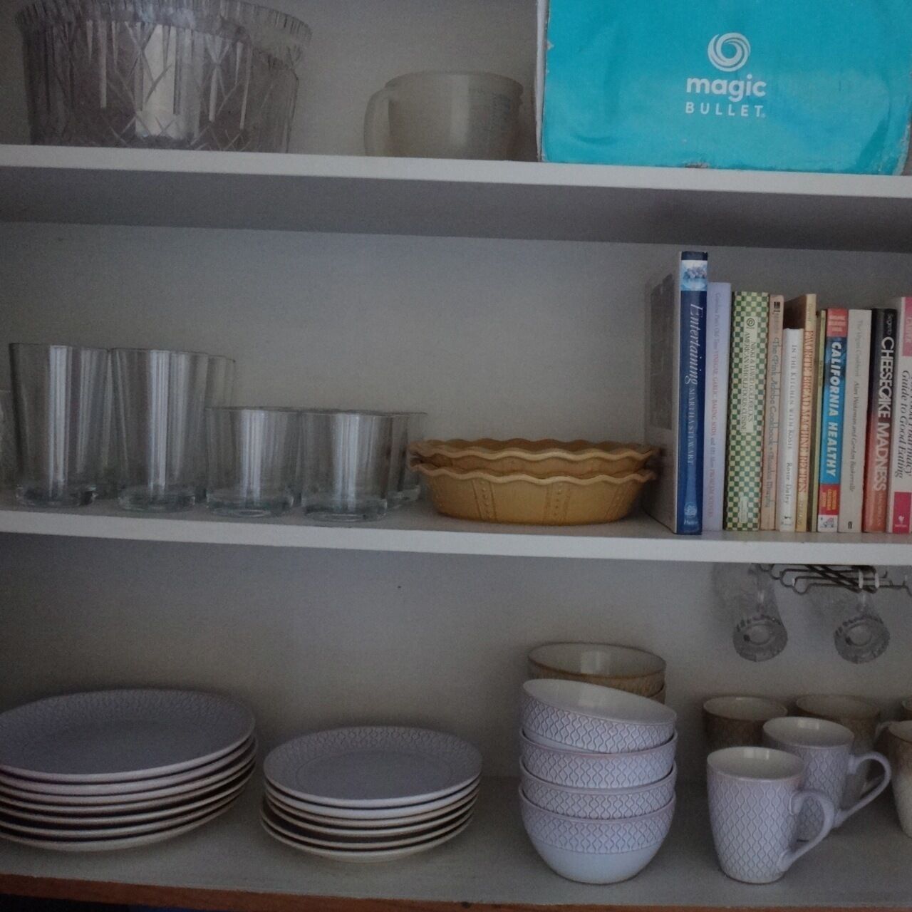 A shelf with various glassware, a pie dish, and a stack of plates.