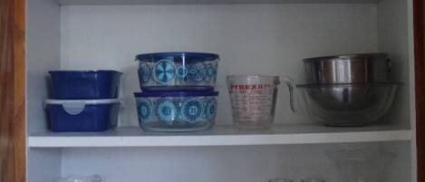 Una estantería de cocina con diversos utensilios, incluyendo tazones, tazas medidoras y recipientes.