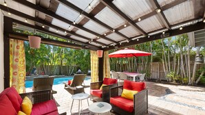 An outdoor patio with wicker furniture, a pool, and a red umbrella. - Martini Manor is the ultimate Tropical Oasis with a private Heated Pool! (Wilton Manors)