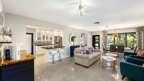 A modern living room with a sofa, coffee table, and chairs. There is a kitchen area with a dining table and chairs. The room has large windows with curtains. - Martini Manor is the ultimate Tropical Oasis with a private Heated Pool! (Wilton Manors)