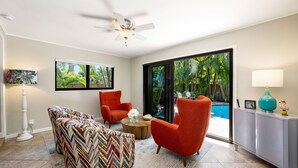 A modern living room with a ceiling fan, a large window with a view of a pool, and a grey cabinet with decorative items. - Martini Manor is the ultimate Tropical Oasis with a private Heated Pool! (Wilton Manors)