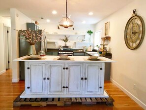 Una cocina con isla central, muebles blancos y una lámpara colgante.