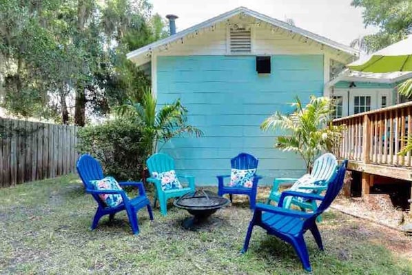 A small blue house with a deck, surrounded by greenery.