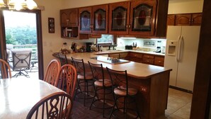 A kitchen with wooden cabinets, a central island with bar stools, a refrigerator, and a dining area with chairs. - Gateway To Pikes Peak, Garden Of The Gods, Manitou Springs, Old Colorado City (Colorado Springs)