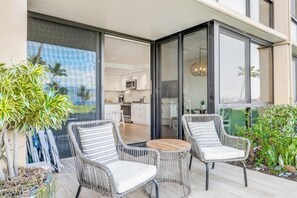 Ein moderner Außenbereich zum Sitzen mit Korbstühlen und einem Holztisch, mit Blick auf eine Wohnküche und ein Wohnraum.