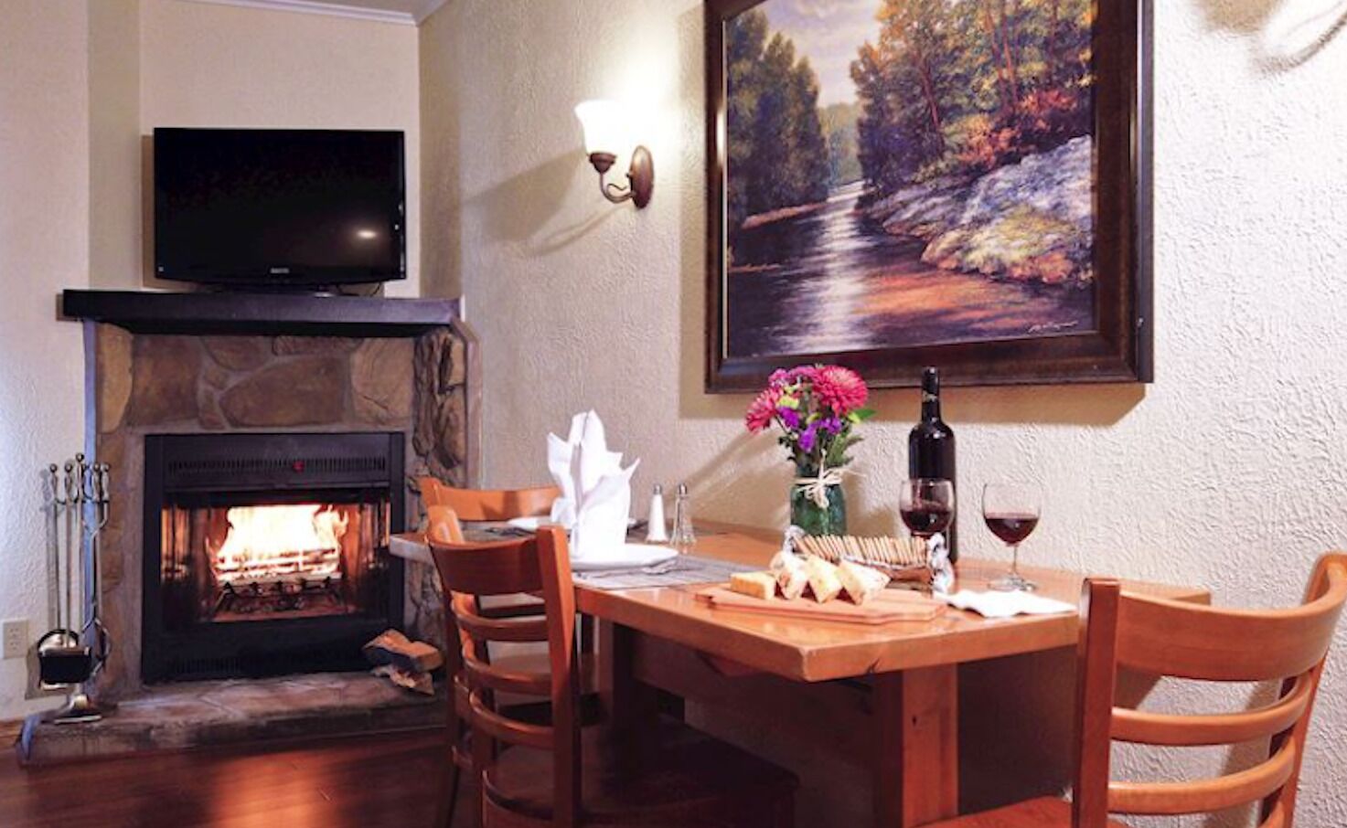 A cozy dining area with a fireplace, a table set for two, and a painting on the wall.