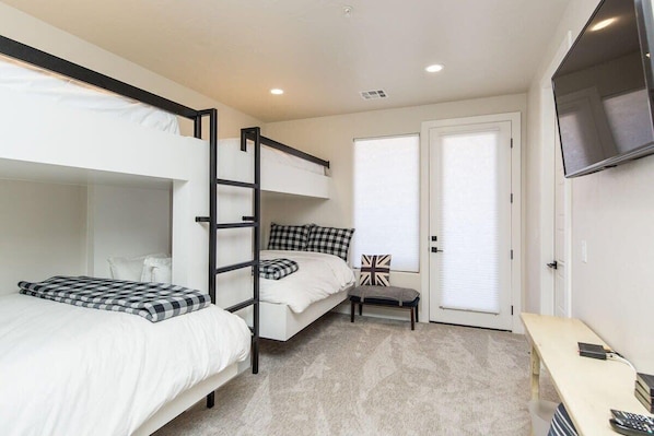 A bedroom with bunk beds, a desk, a chair, a television, and a door with a window.