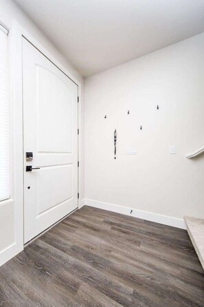 A room with a white door, a light-colored wall, and a dark wooden floor.
