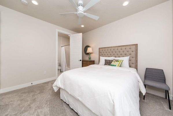 A bedroom with a large bed, a ceiling fan, and a nightstand with a lamp.
