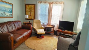 Una sala de estar con un sofá de cuero marrón, un sillón color beige, un televisor y un cuadro grande en la pared.