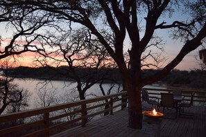 Une terrasse en bois avec une rambarde donnant sur un plan d’eau, un foyer et des sièges d’extérieur.