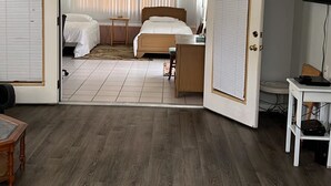 Una habitación con una cama, un escritorio, un televisor y un amplio ventanal con persianas.