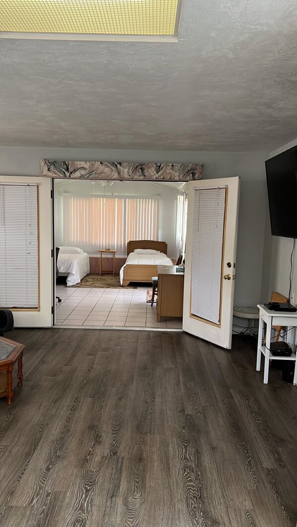 Een kamer met een bed, een bureau, een televisie en een groot raam met jaloezieën.