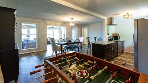 Un grand espace de vie comprenant un salon avec un baby-foot, un coin repas et une cuisine.