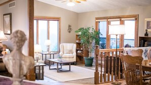 A spacious living room with a large window, a comfortable armchair, a coffee table, and a bookshelf. - Great for Friends & Families, Breathtaking View, Nature Trails, Farm Animals (Millersburg)