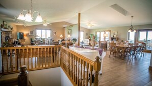 A spacious living area with a wooden staircase, a dining area with chairs and a table, and a kitchen with a fireplace. - Great for Friends & Families, Breathtaking View, Nature Trails, Farm Animals (Millersburg)
