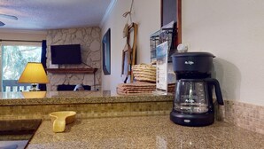 Una cocina con encimeras de granito, cafetera, lavamanos y ventana con vistas a árboles.