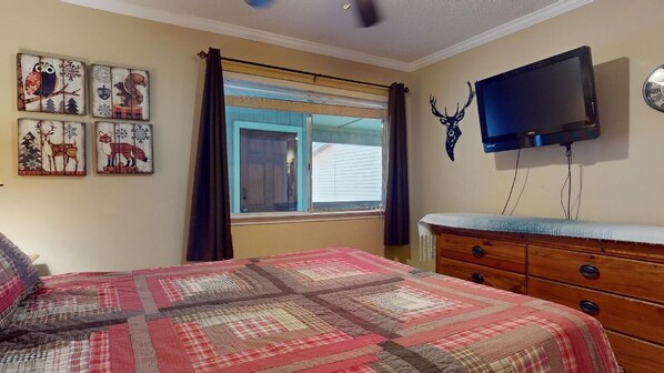 A bedroom with a bed, a dresser, a television mounted on the wall, and a window with curtains.