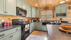 Una cocina con armarios verde claro, estufa negra, microondas y techo de madera.