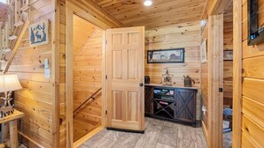 Interior de madera con una puerta de madera, una escalera, un cuadro enmarcado en la pared y una pequeña mesa con una lámpara.