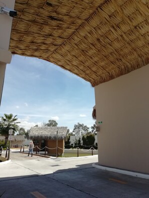 A covered outdoor area with a thatched roof, a small hut, and a paved walkway.