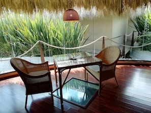 A glass-top table with wicker chairs, a rope barrier, and a view of green plants through a glass wall.