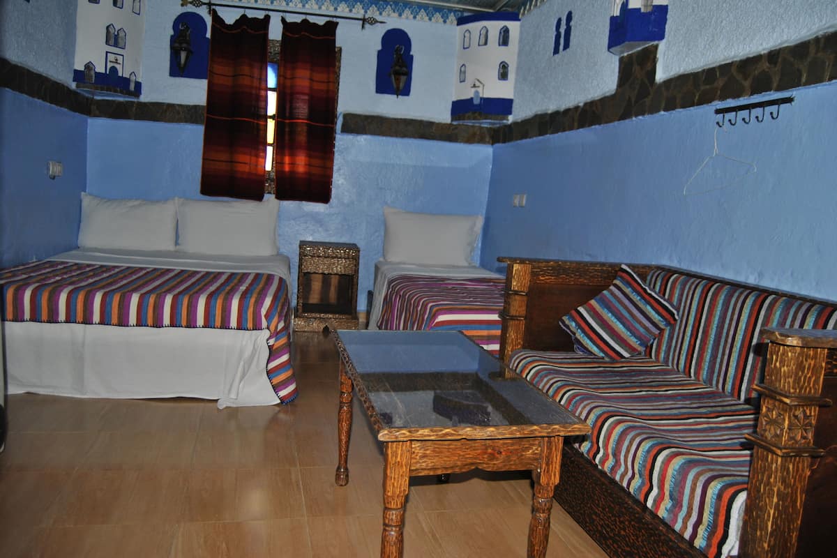 A room with two beds, a sofa, a wooden table, and a patterned wall.