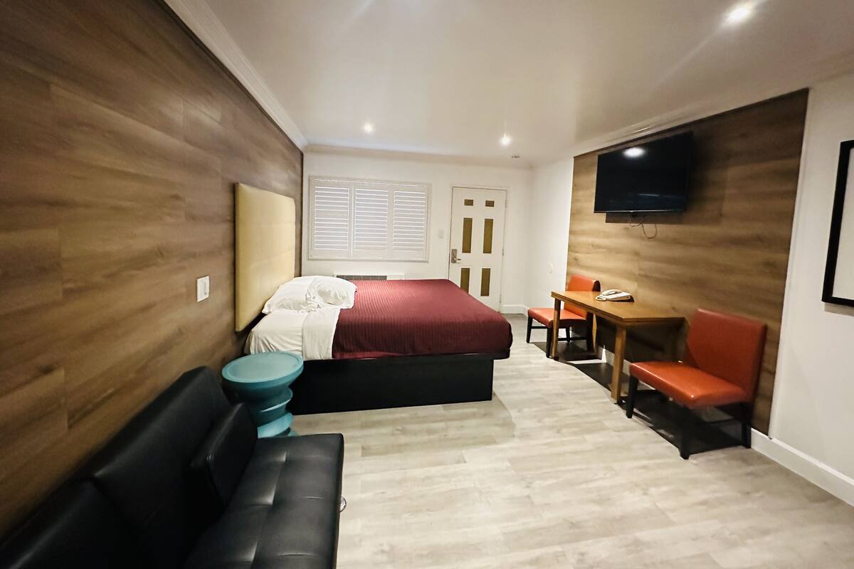 A modern hotel room with a bed, a desk, a chair, and a sofa.