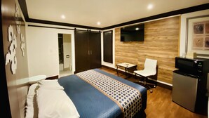 A hotel room with a bed, a desk, a chair, a TV, and a refrigerator. - Casa Blanca Inn & Suites (Whittier)