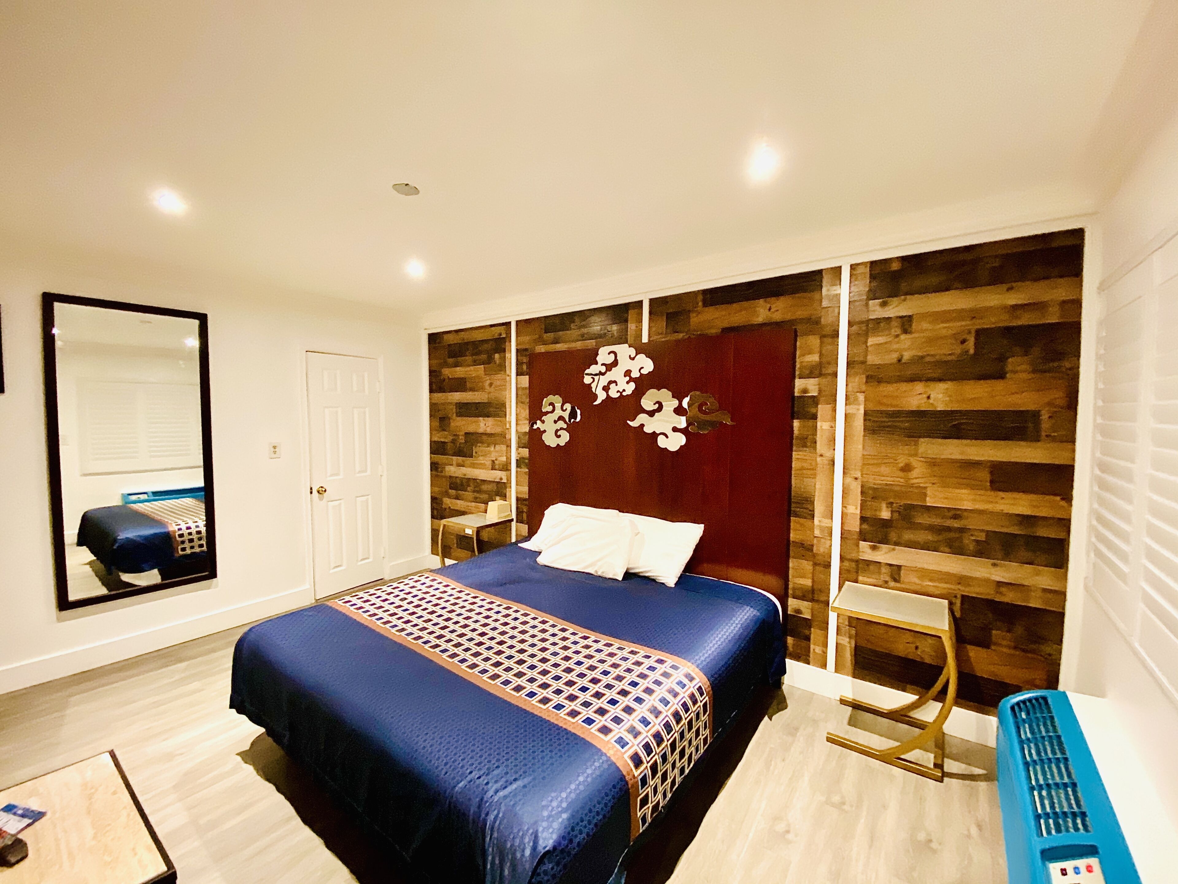 Une chambre avec un grand lit, un mur d’accent en bois, un miroir et un bureau.