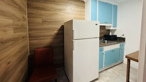 A compact kitchen with a white refrigerator, blue cabinets, and a wooden accent wall. - Casa Blanca Inn & Suites (Whittier)