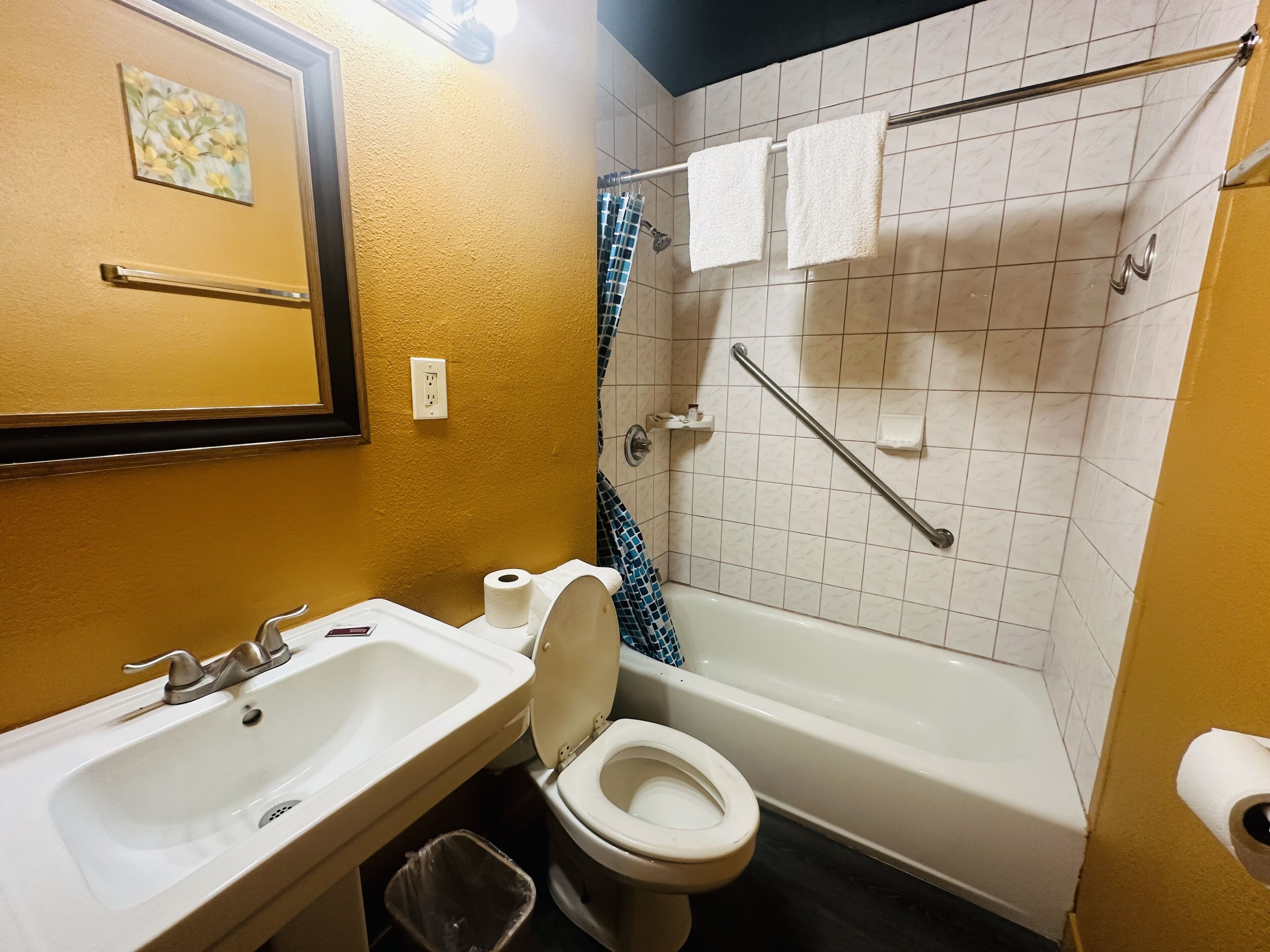 A bathroom with a sink, toilet, and bathtub. There is a handrail in the shower area, and a towel rack above the bathtub.