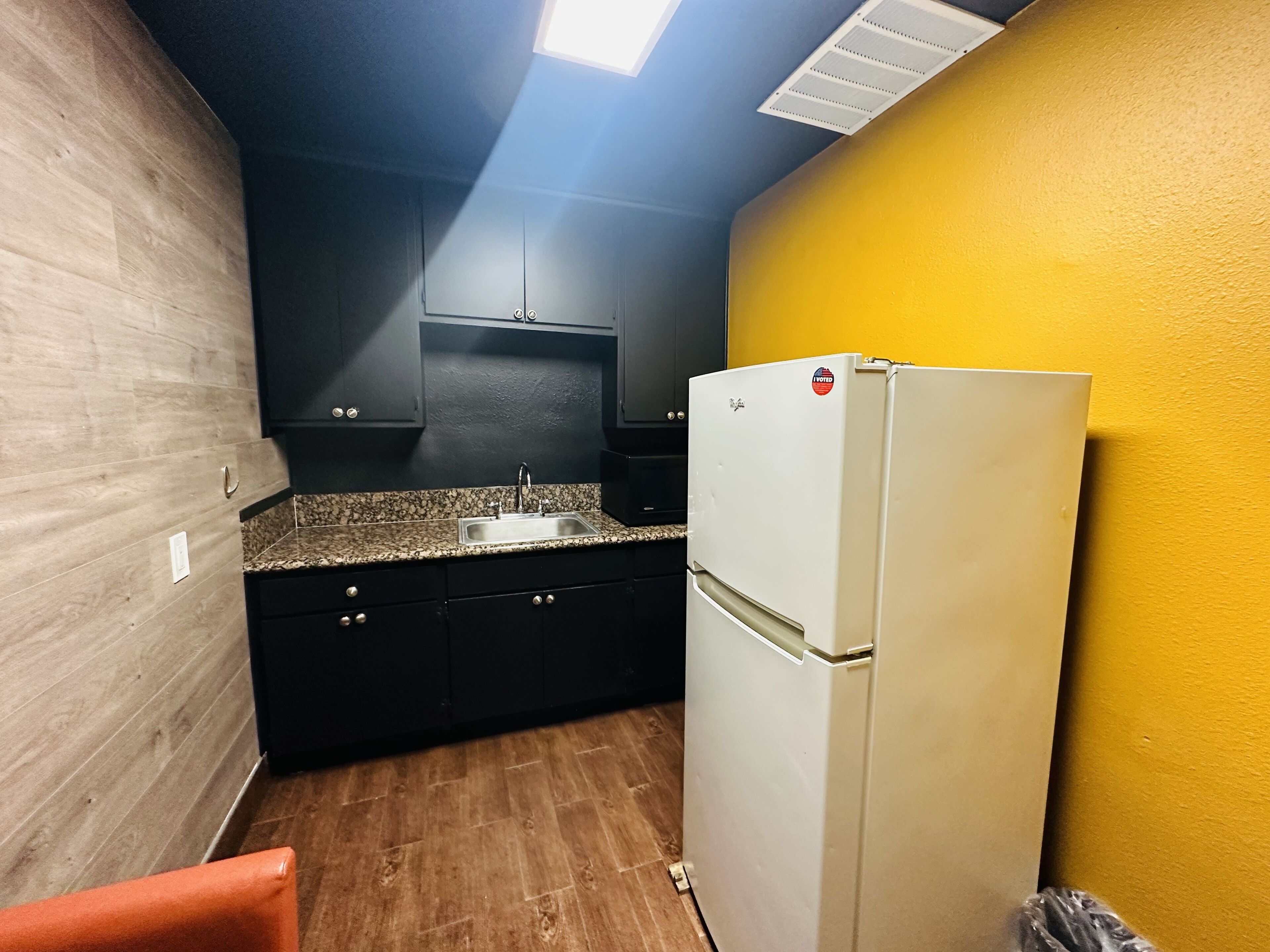 A compact kitchen with dark cabinets, a granite countertop, and a white refrigerator.