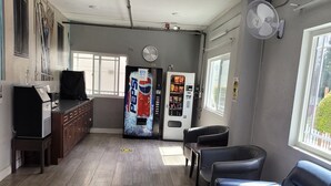 A spacious room with a large couch, a coffee machine, a Pepsi vending machine, and a clock on the wall.
