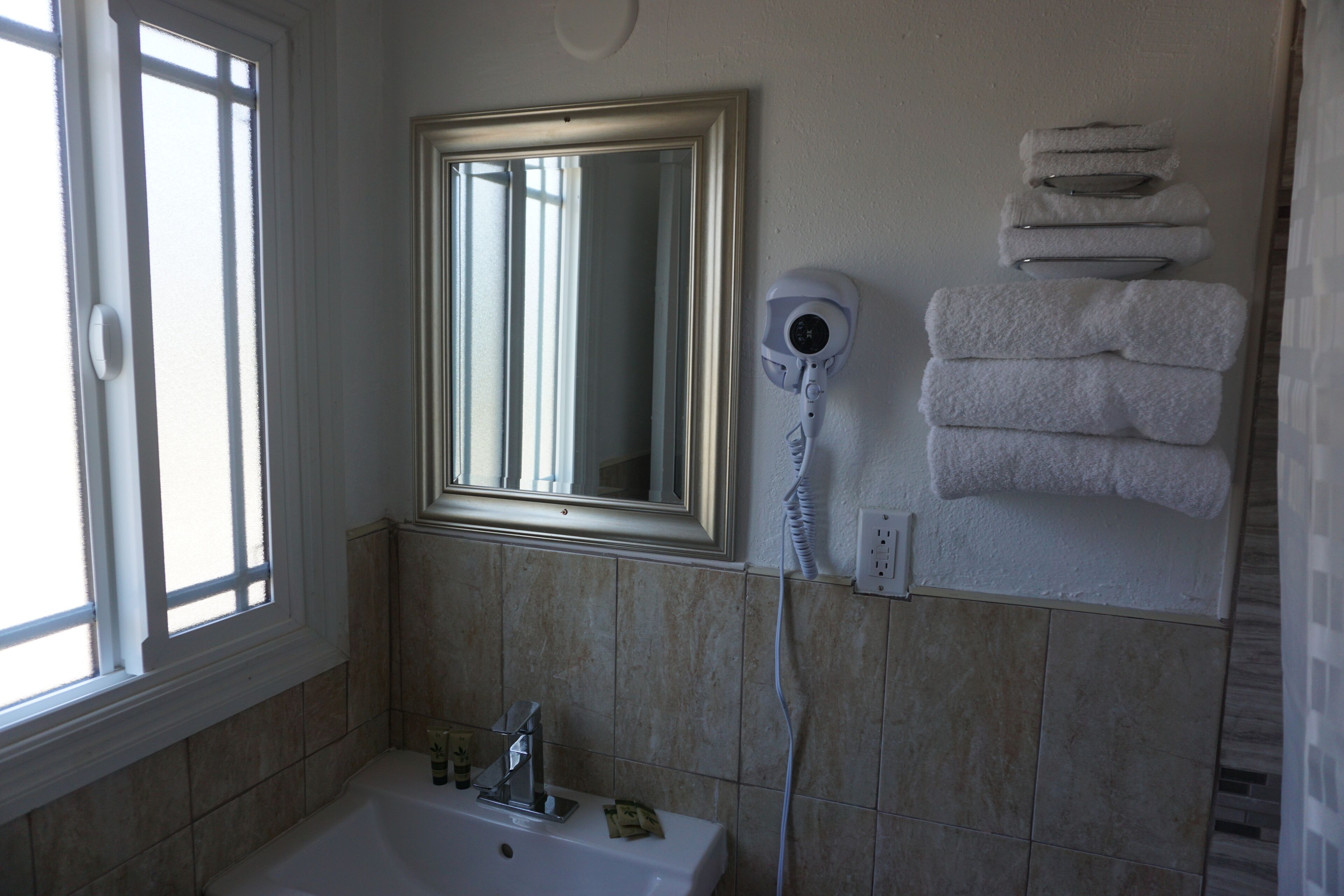 Une salle de bain équipée d’un lavabo, d’un miroir, d’un porte-serviettes et d’un sèche-cheveux fixé au mur.