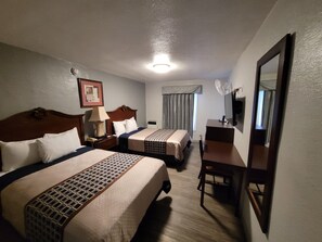 A hotel room with two beds, a desk, a chair, a TV, and a ceiling light. - Las Palmas Hotel (Los Angeles)