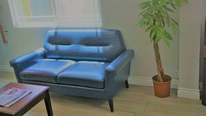 A blue leather sofa with a matching ottoman, a potted plant, and a magazine on a small table.