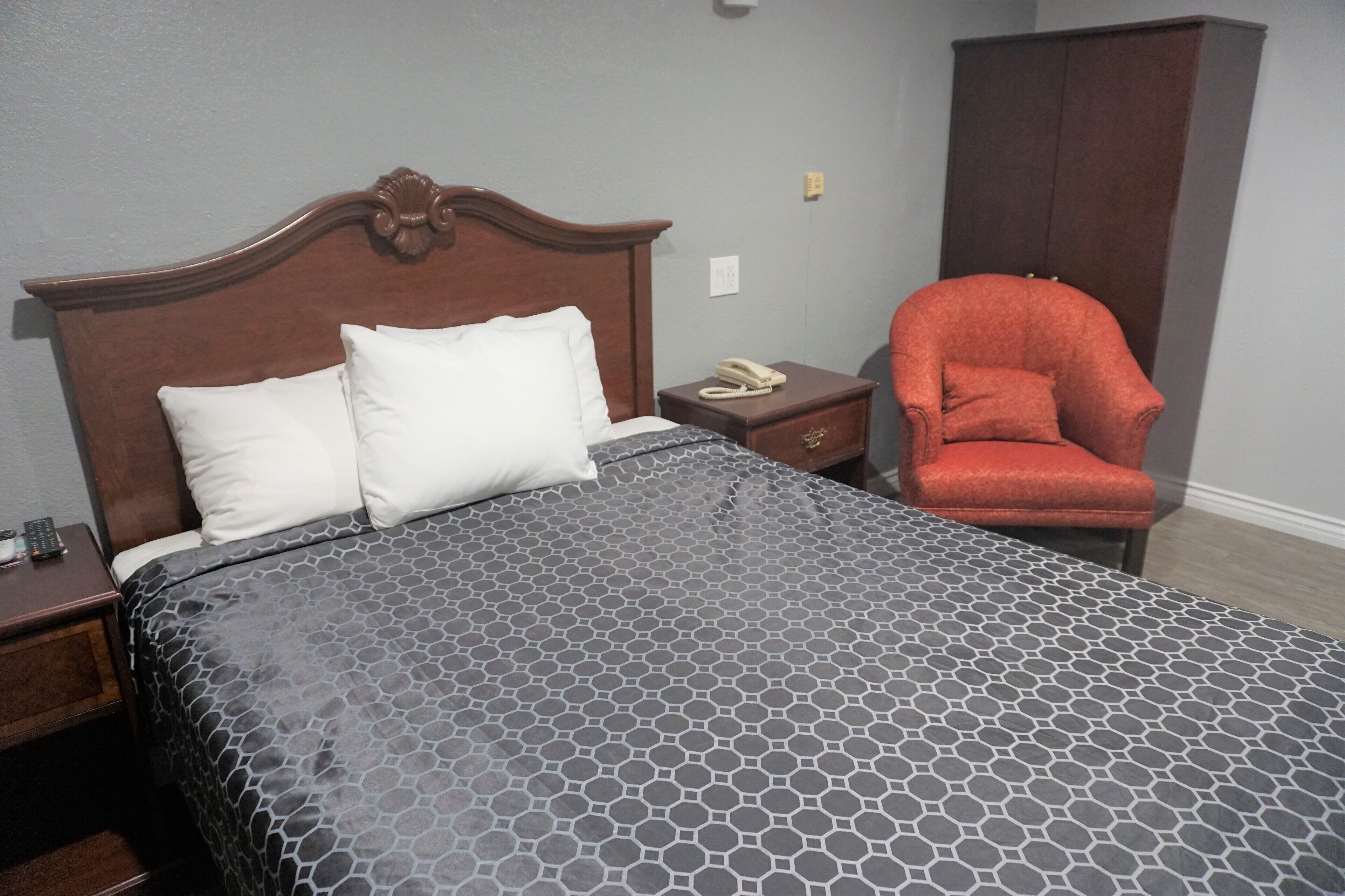 A hotel room with a large bed, a nightstand with a telephone, and a red armchair.